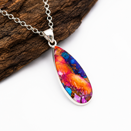 Sterling silver teardrop pendant necklace with copper turquoise stone, angled view on wood